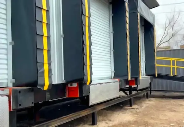 Three-bay modular cross-docking platform showing dock seals, rollup doors, and dock levelers at each bay position, with yellow safety railing and yard ramp approach visible at right.