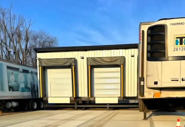 Enclosed modular cross-docking platform with rollup doors and dock seals, refrigerated trailers backed up on both sides for inbound and outbound transfer, Long Island installation.