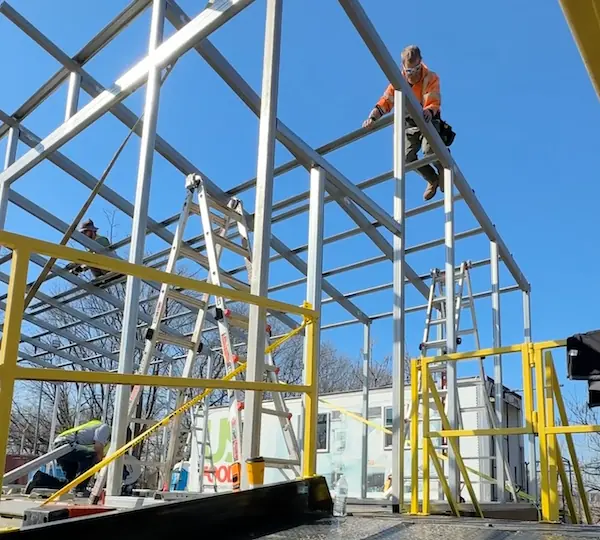 Worker in orange safety vest assembling steel frame of a modular cross-docking platform enclosure on a clear day, Long Island installation.