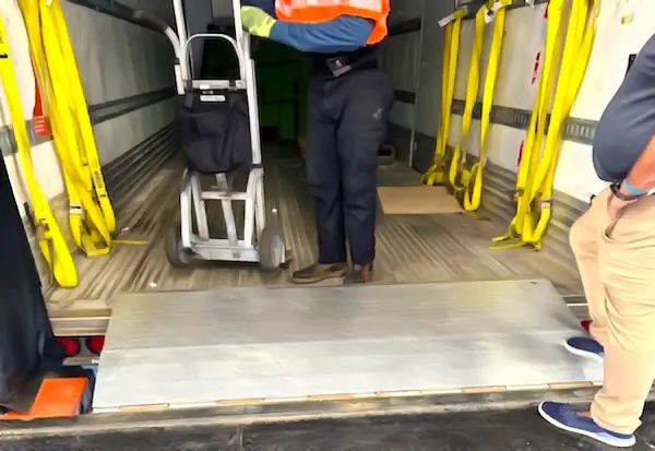 Worker in safety vest using a hand truck to unload freight at a truck bed threshold, modular cross-docking platform installation.